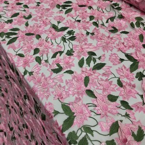 Puede incluir: Tela de encaje bordado floral rosa con hojas verdes. El delicado dise&ntilde;o presenta flores y enredaderas tridimensionales, creando un aspecto texturizado y elegante. Ideal para vestidos, faldas u otras prendas.