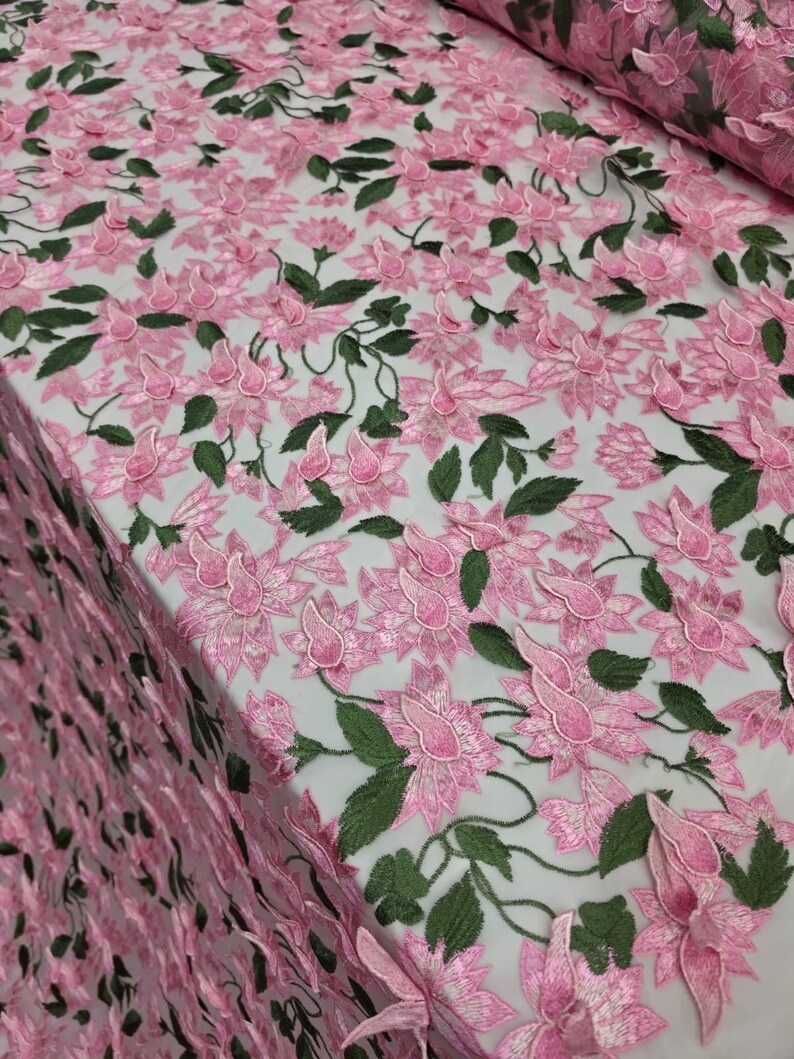 Puede incluir: Tela de encaje bordado floral rosa con hojas verdes. El delicado dise&ntilde;o presenta flores y enredaderas tridimensionales, creando un aspecto texturizado y elegante. Ideal para vestidos, faldas u otras prendas.