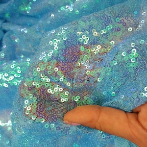 May include: Close-up of a light blue fabric with iridescent sequins. The fabric is sheer and has a delicate texture.