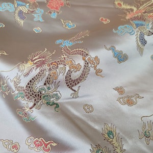 May include: A beige fabric with a repeating pattern of gold, red, and green dragons and peacocks. The fabric has a satin-like sheen.