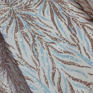 May include: A white fabric with a rose gold and iridescent blue sequin pattern. The pattern is a repeating design of curved lines.
