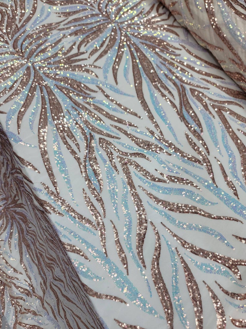 May include: A white fabric with a rose gold and iridescent blue sequin pattern. The pattern is a repeating design of curved lines.