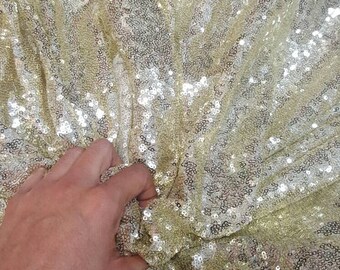 May include: A close-up of a gold sequined fabric. The sequins are small and tightly packed, creating a shimmering effect.