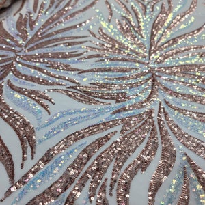 May include: A white fabric with a rose gold and iridescent sequin pattern. The sequins are arranged in a wavy, abstract design.