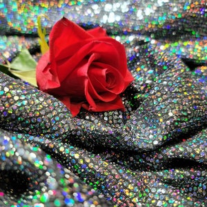 May include: A single red rose with green leaves rests on a silver sparkly fabric background.