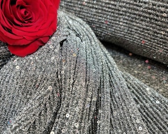 May include: A close-up of a silver fabric with sequins. A red rose is placed on top of the fabric.