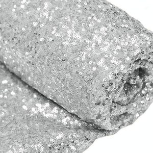May include: Silver sequin fabric, a close-up of the sparkly material. The fabric is rolled up, showing the texture and shine of the sequins.
