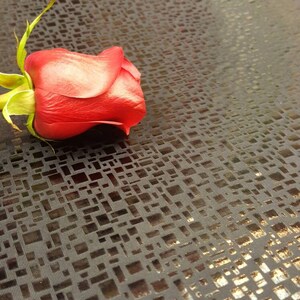 May include: A single red rose lying on a black fabric with a gold metallic pattern.