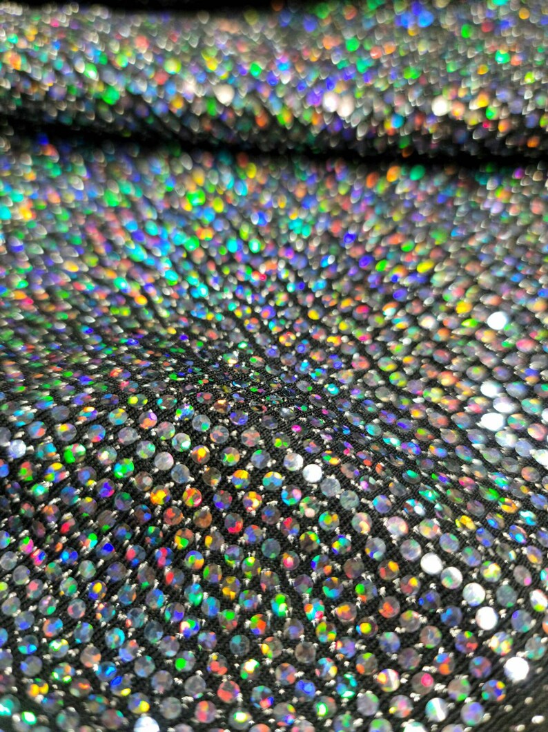 May include: Close-up of iridescent fabric with a pattern of small, round sequins. The sequins are arranged in a repeating pattern and create a shimmering effect.