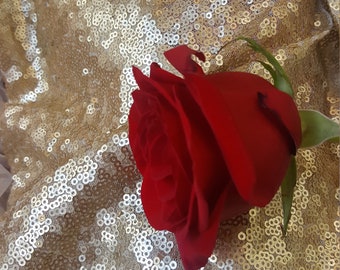 May include: A single red rose with green leaves on a gold sequined background.