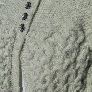 May include: A cream-colored knitted cardigan with a cable knit pattern and a row of silver buttons down the front.