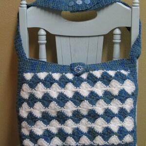 May include: A blue and white crocheted tote bag with a diamond pattern. The bag has a blue strap and a blue button closure.