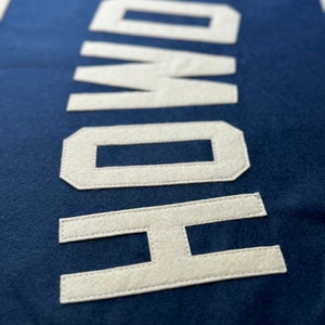 Pu&ograve; includere: Uno stendardo in feltro blu navy con la parola "HOWDY" cucita in feltro bianco.