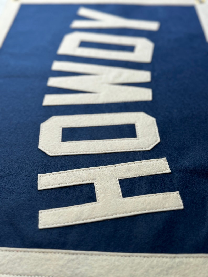 Pu&ograve; includere: Uno stendardo in feltro blu navy con la parola "HOWDY" cucita in feltro bianco.