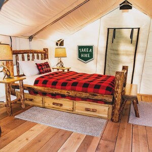May include: A wooden bed frame with a red and black plaid blanket and a sign that says "Take a Hike". The bed is in a tent with a wooden floor.
