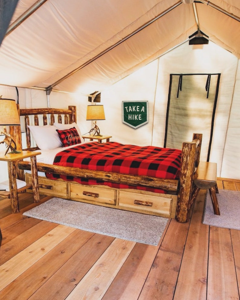 May include: A wooden bed frame with a red and black plaid blanket and a sign that says "Take a Hike". The bed is in a tent with a wooden floor.