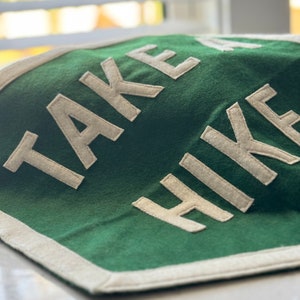 May include: A green felt pennant with white felt lettering that reads "TAKE A HIKE".