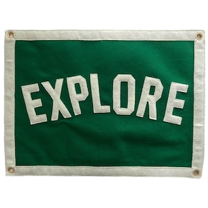 May include: A green felt banner with white felt lettering that reads "EXPLORE". The banner has a white border.