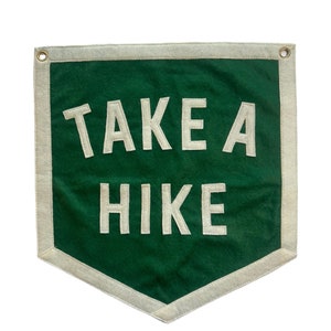 May include: A green felt pennant with white stitching and a white border. The pennant has the text "TAKE A HIKE" in white.