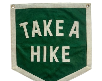 May include: A green felt pennant with white stitching and a white border. The pennant has the text "TAKE A HIKE" in white.