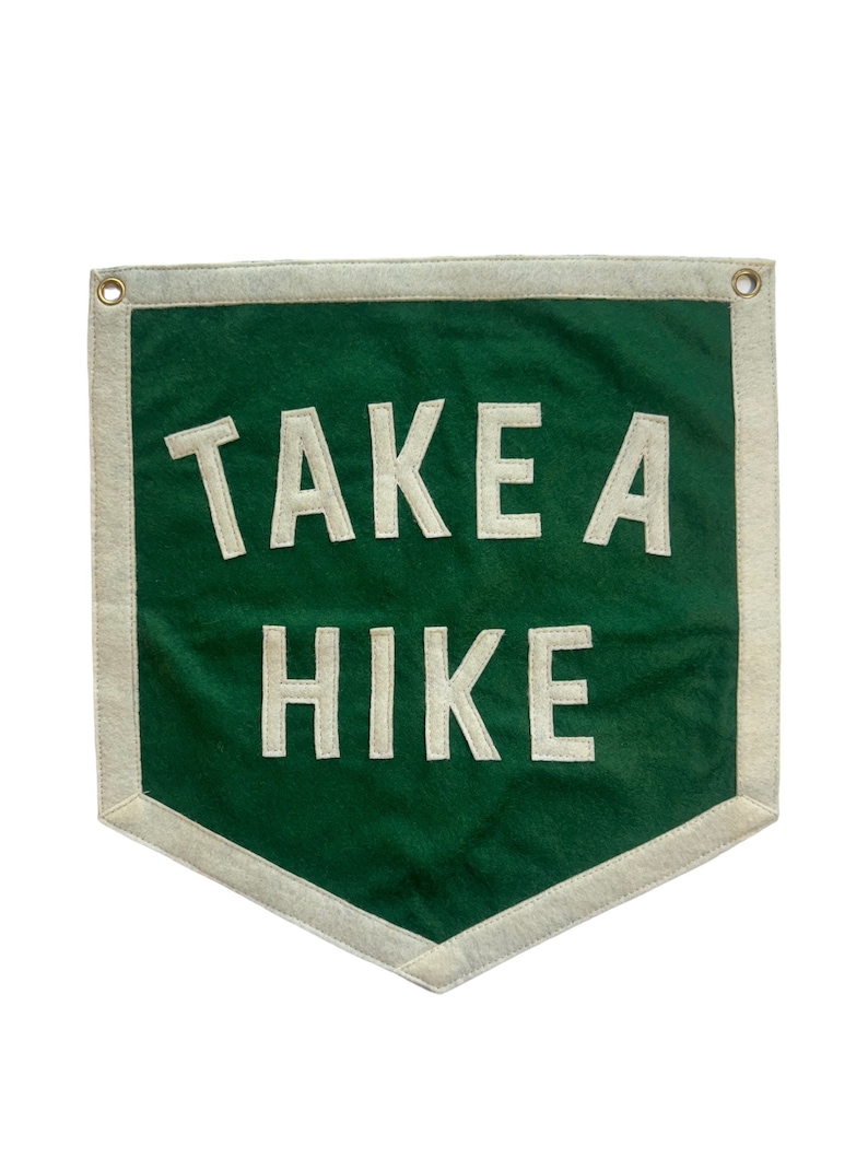 May include: A green felt pennant with white stitching and a white border. The pennant has the text "TAKE A HIKE" in white.