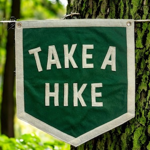 May include: A green fabric banner with white text that reads "TAKE A HIKE" hanging from a tree branch.