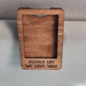May include: A wooden car visor clip with the text "Buckle Up! We Love You!" engraved on it.