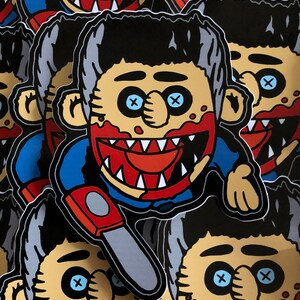 May include: A stack of stickers featuring a cartoon character with black hair, blue eyes, and a red, toothy grin. The character is wearing a blue shirt and holding a gray chainsaw. The stickers have a black background.