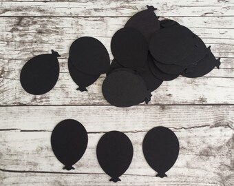 May include: Black paper cutouts of balloons on a white wood background.