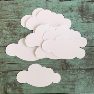 May include: A stack of white paper clouds on a green wooden background. The clouds are cut out in a simple shape and are arranged in a staggered pattern.