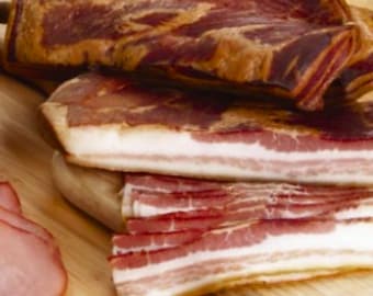 May include: Close-up of a stack of thinly sliced, cured bacon on a wooden cutting board. The bacon is a deep red color with a slight sheen and has a marbled appearance.