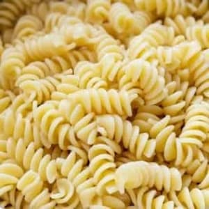 Puede incluir: Primer plano de un bol de pasta rotini cocida. La pasta es de color amarillo dorado y tiene un acabado ligeramente brillante.