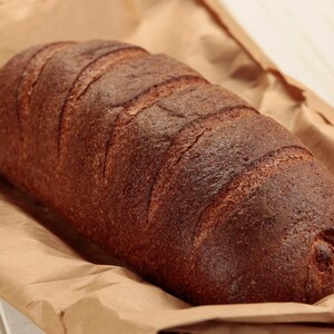 Puede incluir: Una hogaza de pan marrón oscuro con una corteza crujiente, sentada sobre una bolsa de papel marrón.