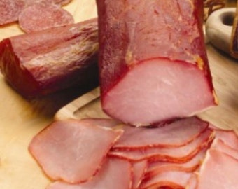 May include: Close-up of thinly sliced cured meat, arranged in a fan shape. The meat is a deep red color and has a slightly pink hue. The meat is arranged on a wooden surface.