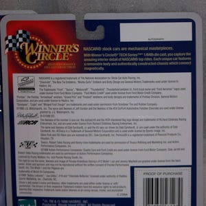 May include: Back of a Winner's Circle die-cast collectible NASCAR car package. The package features text about the car's features, trademarks, and a barcode. The package is blue, red, and white.