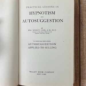 Peut inclure: Un livre ouvert intitul&eacute; "Practical Lessons in Hypnotism and Autosuggestion" par Wm. Wesley Cook. La couverture du livre est blanche avec du texte noir. Le texte "Autosuggestion Applied to Selling" est &eacute;galement visible. Publi&eacute; par Willey Book Company, New York.