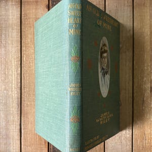 May include: A vintage hardcover book titled An Old Sweetheart of Mine by James Whitcomb Riley, featuring a sage green cloth cover with gold lettering, decorative green leaf motifs, and a central oval portrait of a person on the front cover.