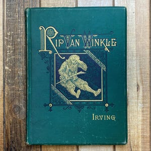 May include: A vintage hardcover book titled "Rip Van Winkle" by Irving. The cover is a deep teal green with gold lettering and an illustration of a man. The book has a worn appearance, suggesting its age.