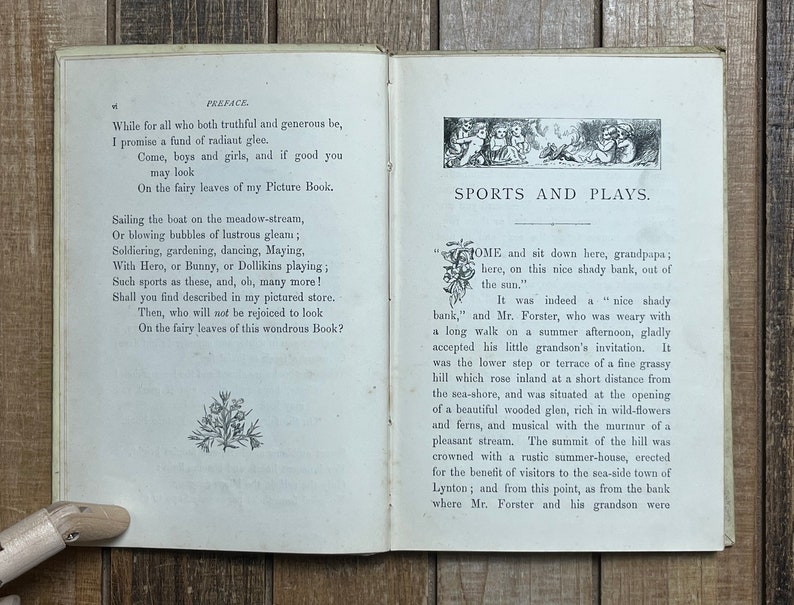 May include: An open book with a white background and black text. The book is titled "Sports and Plays." The text on the page describes a scene of a grandfather and grandson sitting on a shady bank.