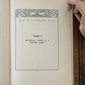 May include: An open book page featuring the title ALL IN A GARDEN FAIR, Chapter I, and the text BOTANICAL NAMES AS A WINTER SPORT. The page includes a decorative green floral border at the top and the number 1 at the bottom center of the page.