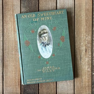 May include: A green hardcover book titled An Old Sweetheart of Mine by James Whitcomb Riley, illustrated by Howard Chandler Christy. The cover features a central oval portrait of a person with a bow tie, surrounded by a decorative floral vine design.