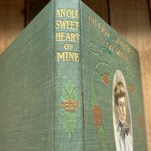 May include: A green hardcover book titled An Old Sweetheart of Mine by James Whitcomb Riley. The spine and cover feature gold embossed lettering and decorative red and green floral illustrations, with an oval portrait of a person on the front.