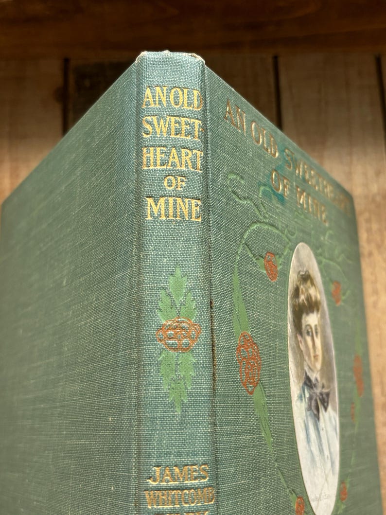 May include: A green hardcover book titled An Old Sweetheart of Mine by James Whitcomb Riley. The spine and cover feature gold embossed lettering and decorative red and green floral illustrations, with an oval portrait of a person on the front.
