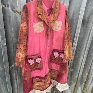 May include: A long-sleeved button-down coat in shades of pink and burnt orange, featuring floral patterned sleeves, two chest pockets with beige lace trim, two lower pockets with pink crochet accents, and a beige lace hemline.