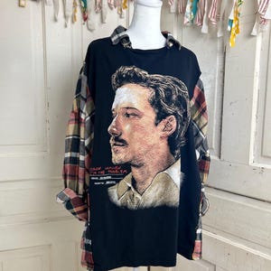 May include: A black long-sleeve shirt featuring a graphic portrait of a man in profile. The shirt has a plaid collar and plaid sleeves. The graphic includes the text MORGAN WALLEN I'M THE PROBLEM, ISSUED 05/18/2021, and DOCKET NO. MW-LP-04.