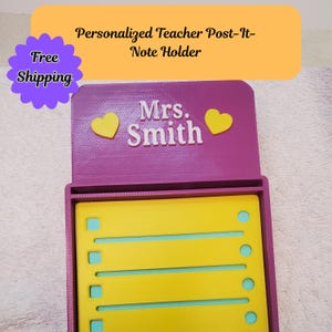 May include: A personalized teacher Post-It note holder in purple with the name "Mrs. Smith" in white. The holder has yellow heart accents and a yellow Post-It note pad. The top of the holder has the text "Personalized Teacher Post-It-Note Holder".