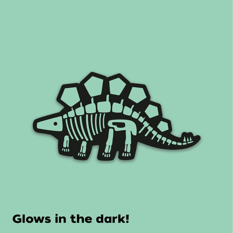 K&ouml;nnte beinhalten: Schwarze Silhouette eines Stegosaurus-Skeletts mit einer Leucht-im-Dunkeln-Funktion. Der Dinosaurier hat einen stacheligen R&uuml;cken und einen langen Schwanz. Der Text "Glows in the dark!" befindet sich unter dem Bild.