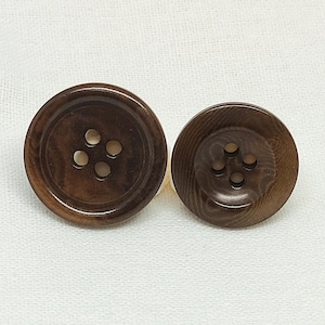 May include: Two brown wooden buttons with four holes each. The buttons are round and have a slightly raised edge.