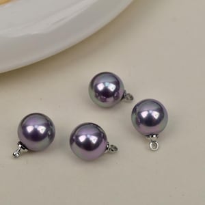 Op de afbeelding: Vier iriserende paarse parel kralen met zilverkleurige bevestigingen. De parels hebben een ronde vorm en een glanzende afwerking. De kralen liggen op een lichtgekleurd oppervlak.