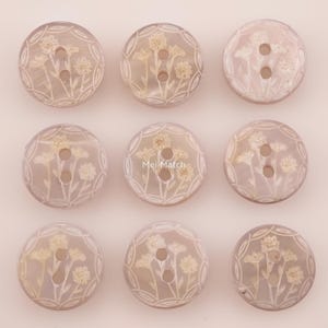 May include: A set of nine round, translucent, light-toned buttons arranged in a three-by-three grid. Each button features a two-hole center and an engraved floral pattern with stems and blossoms. The text Mei Match is visible on the center button.